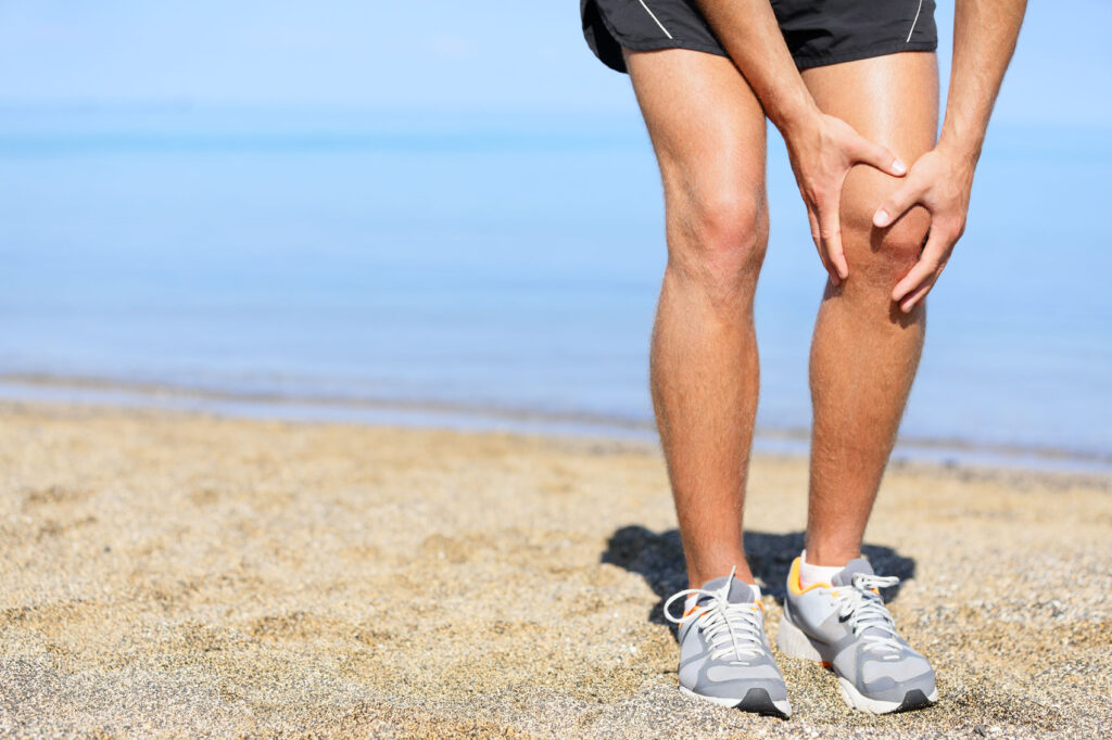 Man in running shorts and shoes holding his left knee in pain.