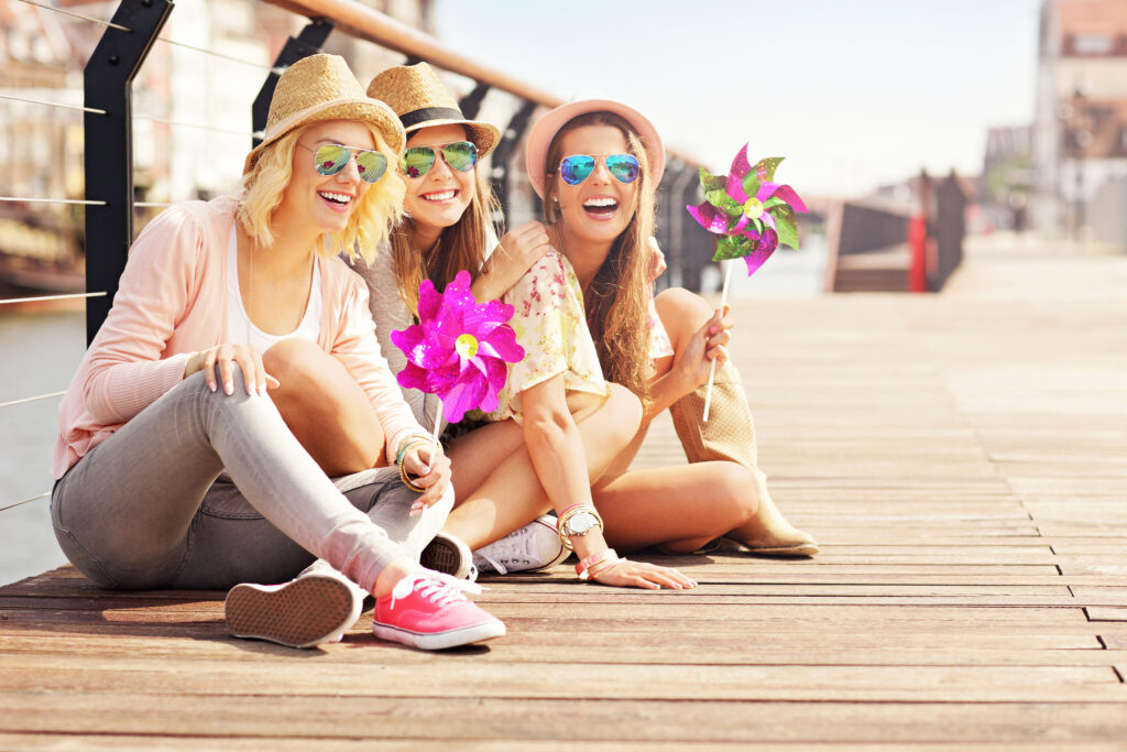 Three women are smiling while sitting on a boardwalk.