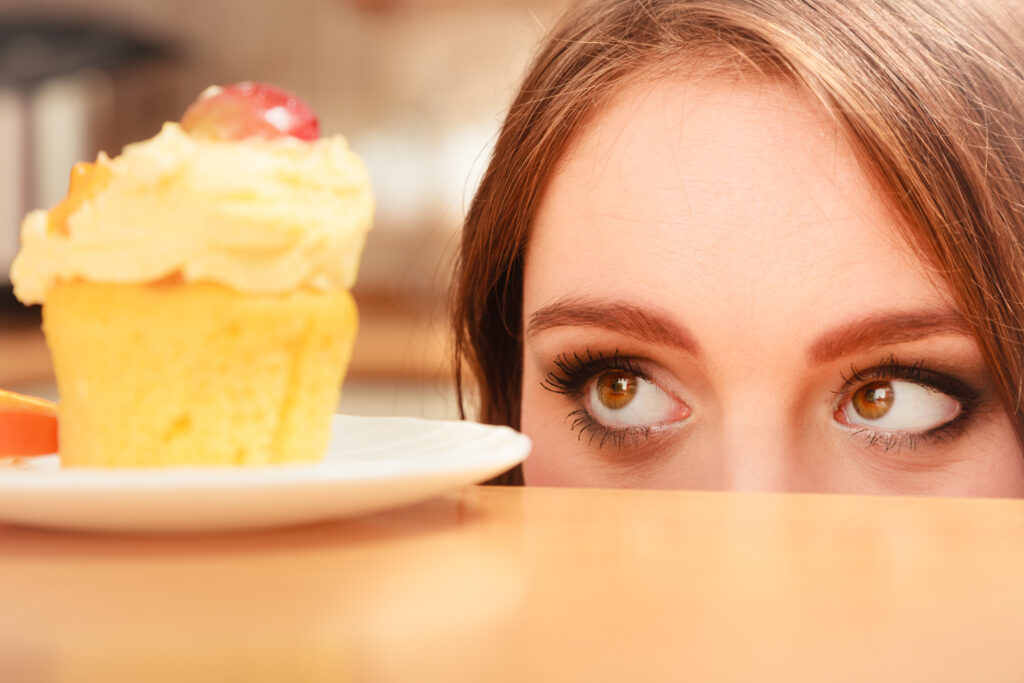 Woman looking at delicious cake with sweet cream and fruits on top. Appetite and gluttony concept.